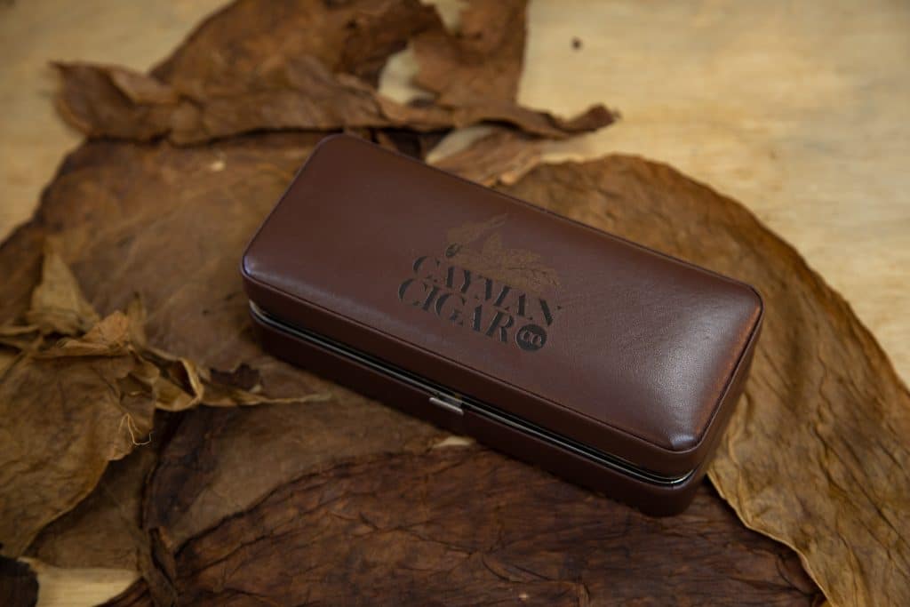 A 'Cayman Cigar Company' leather cigar case sitting on some tobacco leaves.