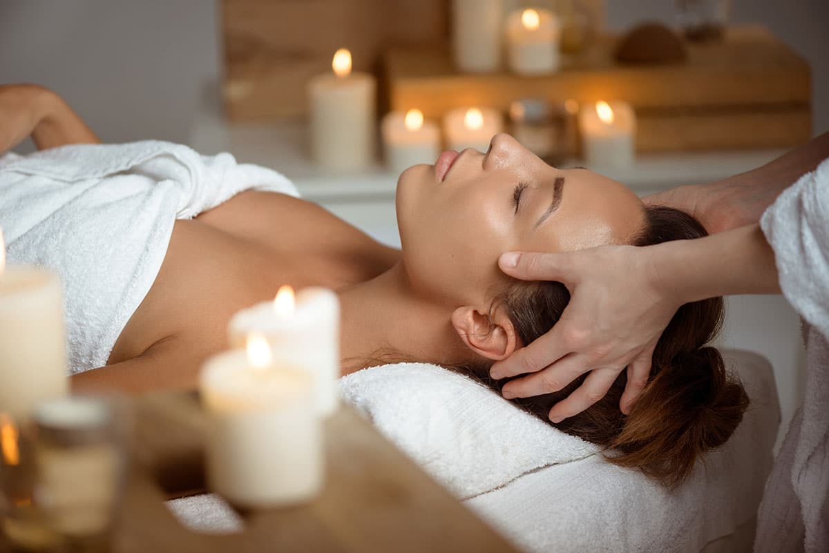 A woman having a head massage in a candle lit room.