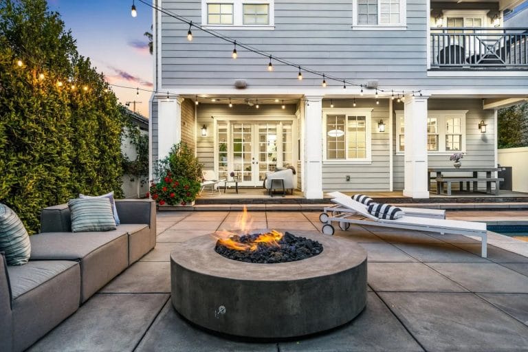 Circular fire pit with colonial style wood panelled property in the background.