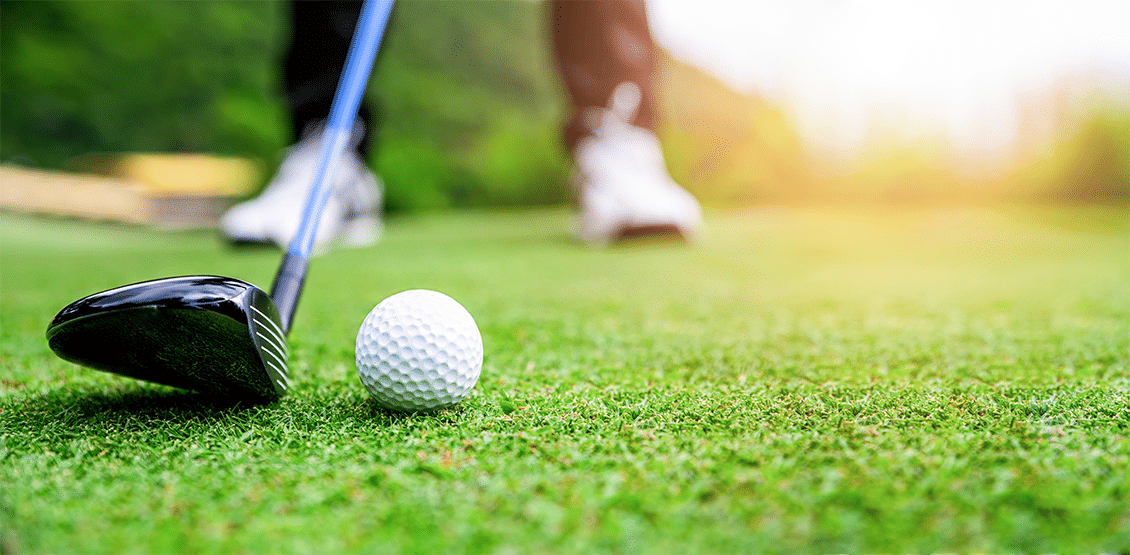 A driver being lined up to a golf ball on a golf course.