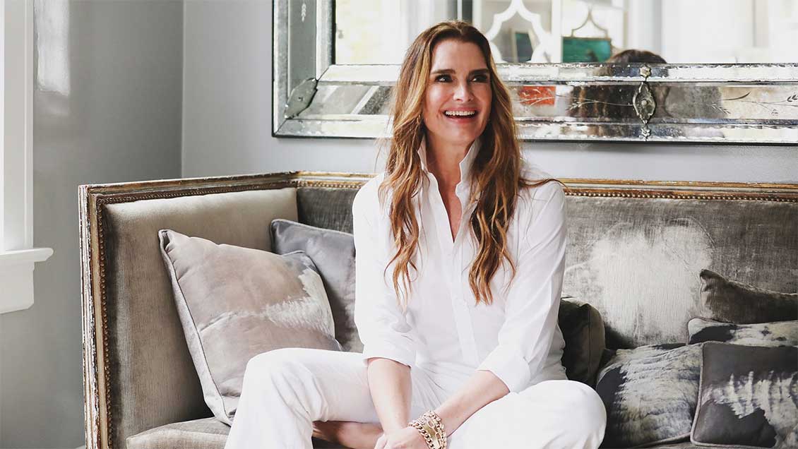 Brooke Shields seated on a velvet couch at her home in the Hampton's discussing the 5 items she couldn't live without.