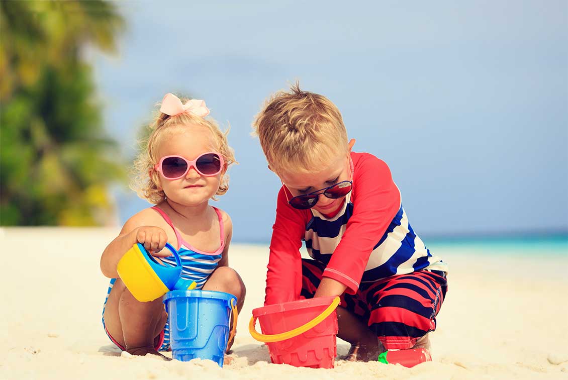 Two kids playing on the beach with buckets and watering cans.