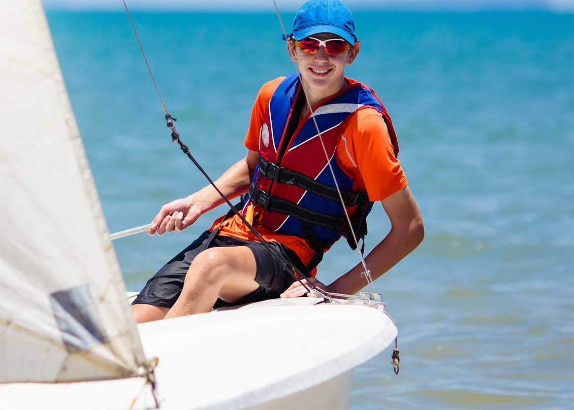 A teenage boy sailing a dinghy on the ocean.
