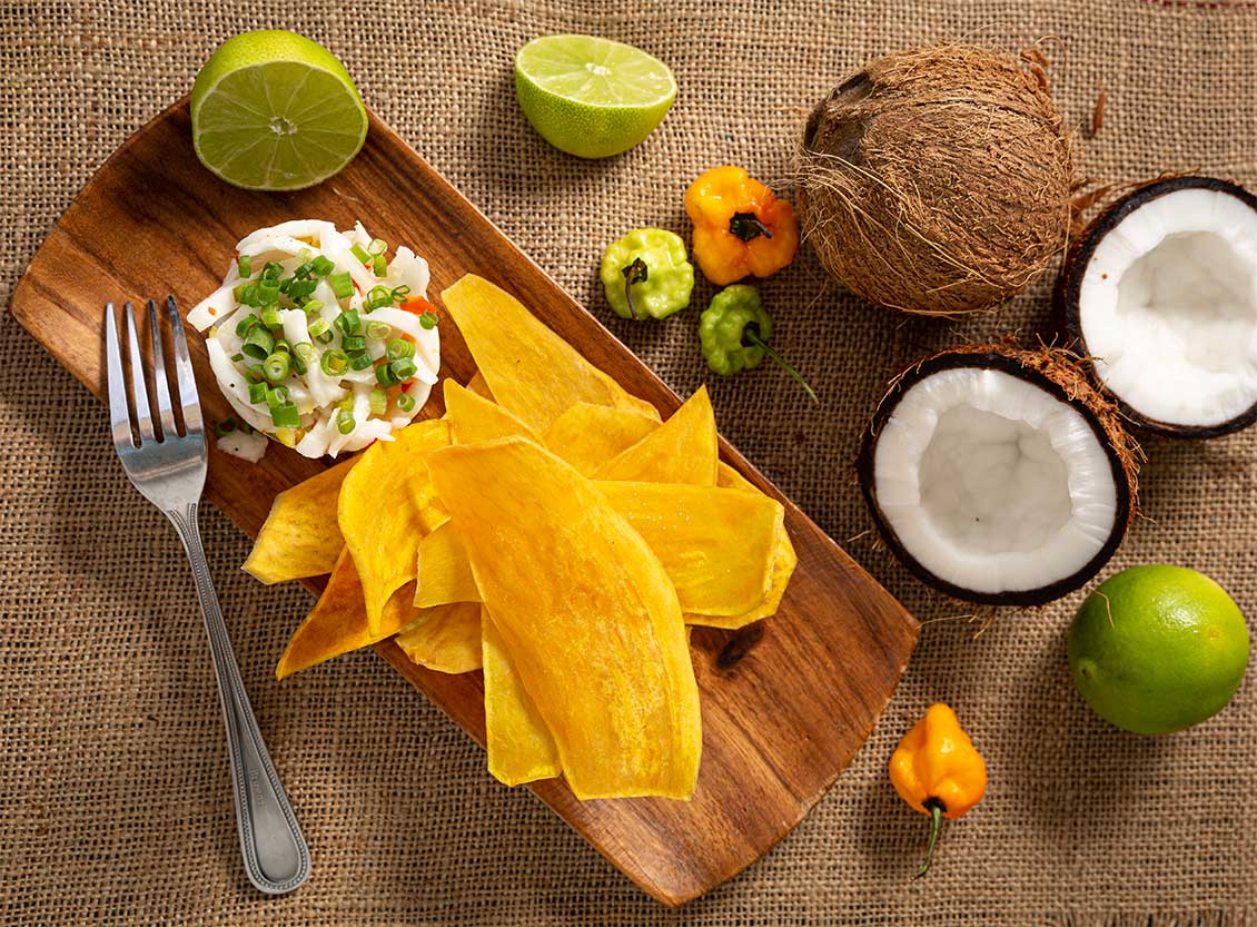 An aerial view of a wooden plate with ceviche, plantain chips, lime and scotch bonnet peppers.