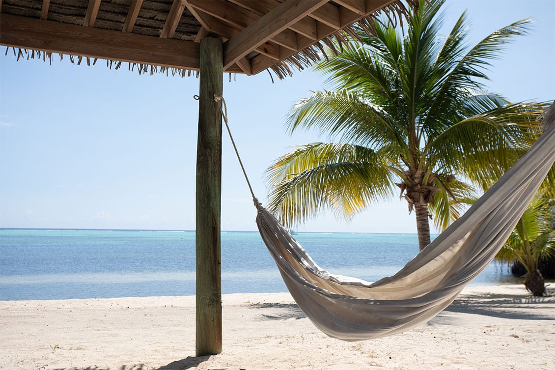 Hammock tied to a beach hut in Little Cayman with the Caribbean Sea in the background.