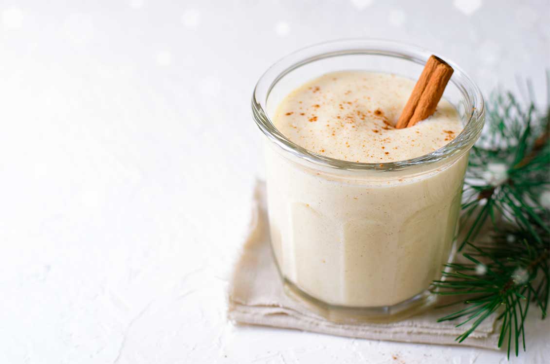 A cup of eggnog with sprinkle of cinnamon and a cinnamon stick,