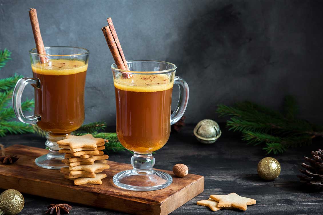 Two glasses of buttered rum with cinnamon sticks and star shaped cookies