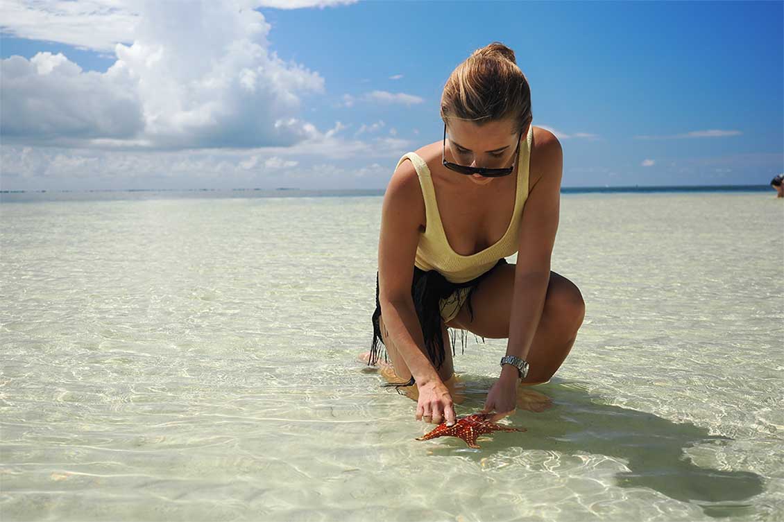 Lady in the shallow waters of Starfish Point touching a starfish.