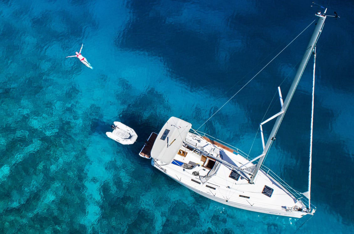 Overhead shot of a sailboat and a woman floating on the Caribbean Sea.