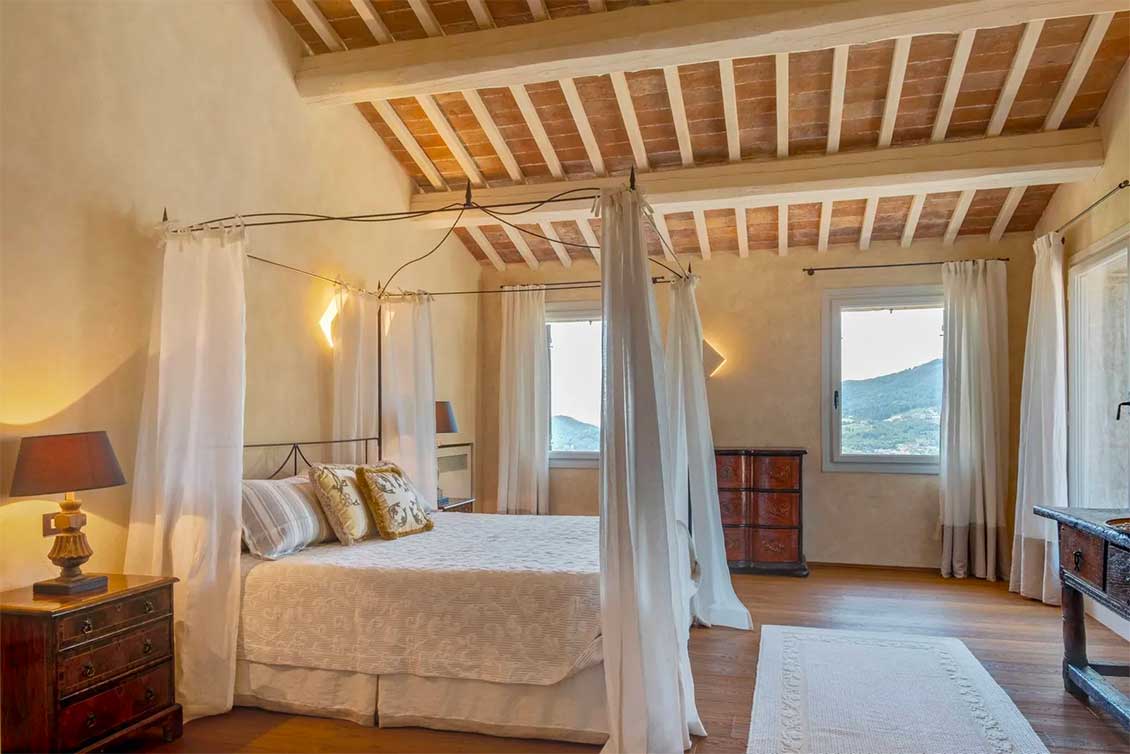 Bedroom with a four poster bed with drapes and cushions designed to inspire hygge.