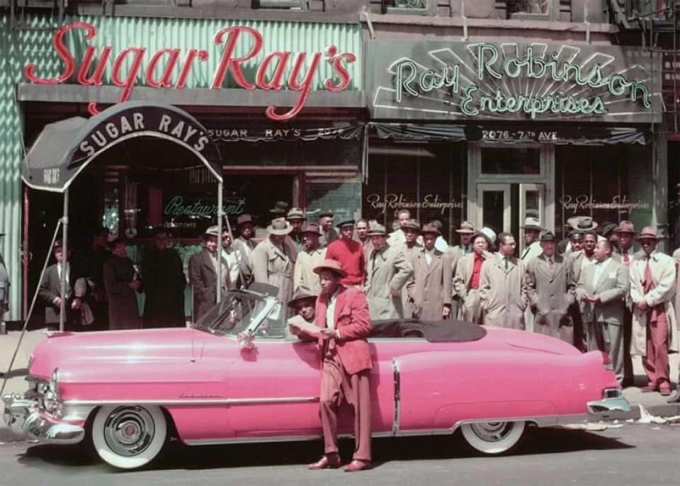TWENTIETH CENTURY FOX. SUGAR RAY ROBINSON LEANING ON HIS 1950 PINK CADILLAC IN FRONT OF TWO OF HIS BUSINESSES IN HARLEM, NEW YORK.